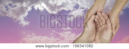 Caring in the Community Charity banner -  wide banner with a woman's hands holding a man's cupped hands in a needy gesture on a beautiful pink and blue sky background  with copy space on the left