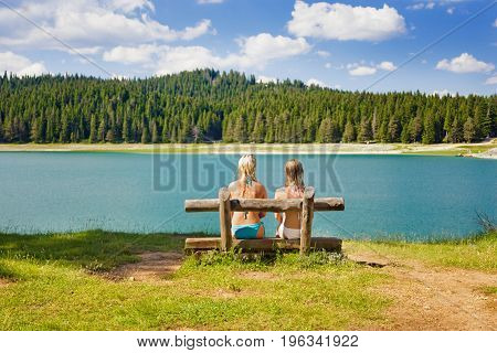 rear view of two girls on a bench made of logs near the lake
