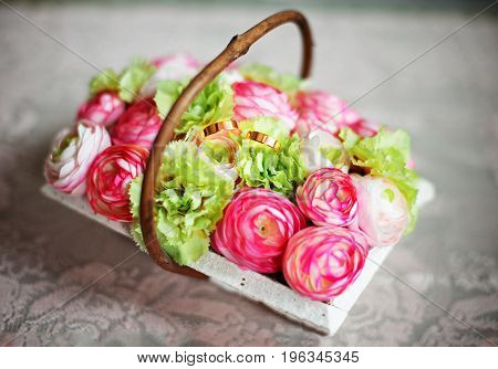 Basket of pink roses and two bridal rings lying inside of it.