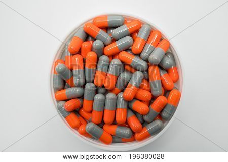 Top view of grey orange capsule pills in plastic container on white background