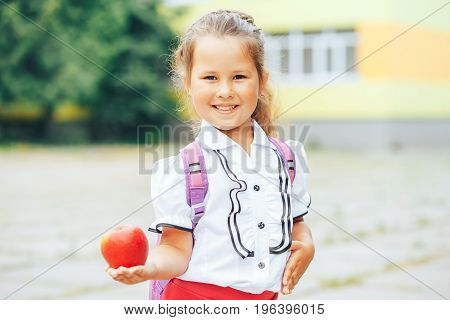 Cute Asian-looking girl holding an apple in the hand on a school background. The girl goes to school