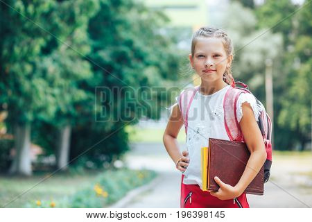 Smiling little girl goes to school with a book and holds book in her hand