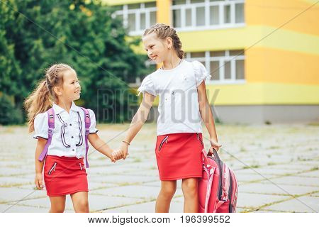 The older sister takes the younger from school. Two schoolgirls go for hands