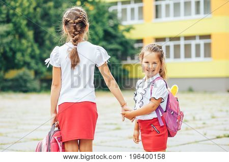 The older sister takes the younger from school. Two schoolgirls go for hands