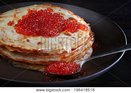 Traditional Russian pancakes with red caviar on a black plate