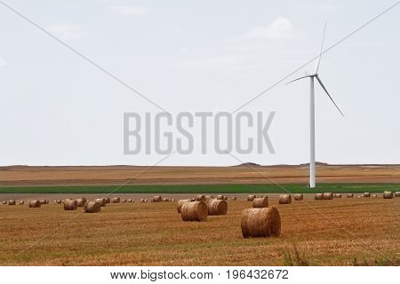 horizontal view of eolian wind turbine on a meadow with wheat hay rolls on a sunny day blue sky with clouds