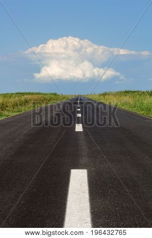 vertical perspective view of black asphalt road with a large white cloud at the horizon against a blue sky