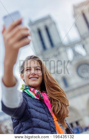 Teenager tourist girl is taking selfie on cathedral of Notre Dame de Paris with mobile smart phone. Travel, tourism, vacation concept. France.