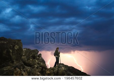 Lonely female trekker admiring mountain view from the top during lightening storm