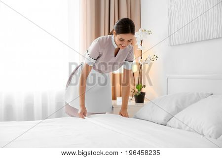 Young maid making bed in light hotel room