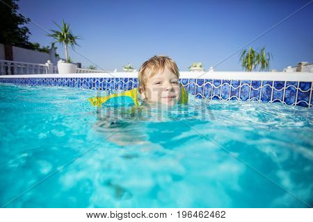 Happy blonde boy wearing floaties and swimming in outdoor pool