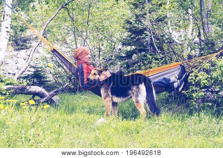 Man Traveler Is Relaxing In Hammock And Playing With His Dog