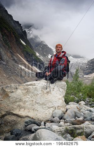 Bearded Man Adventurer Sits On The Stone In The Mountain Gorge