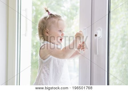 Small child opens window with key. girl is standing on window sill by window. Window with lock.