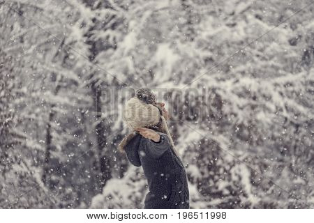 Retro effect faded and toned image of a woman celebrating winter standing outdoors in falling snow with her arms outspread.