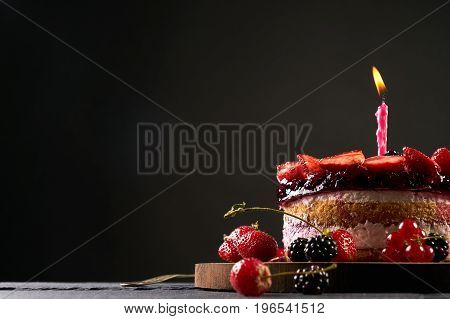 Wodden cake board with homemade raspberry-blackberry and strawberry birthday tart on dark stone table isolated on black background with copy space.