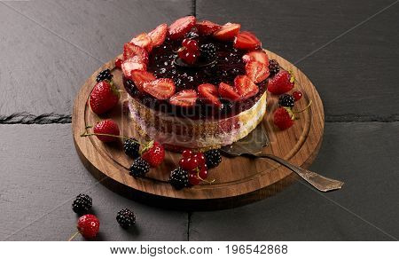 Fresh creamy patisserie cake with raspberries blackberries and strawberries on top. Dark stone background closeup.
