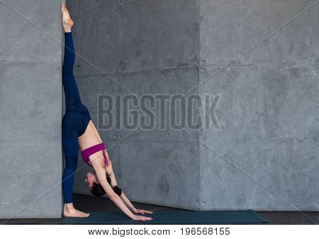 Professional gymnast doing warming-up stretching exercise performing standing split against wall in studio.