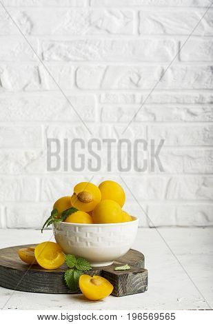 Yellow plums in a white ceramic bowl against a white kitchen brick wall. Selective focus