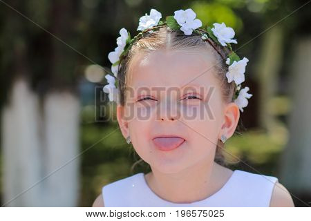Little girl shows tongue child with wreath of artificial flowers on head