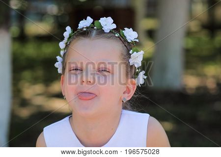 Little girl shows tongue child with wreath of artificial flowers on head