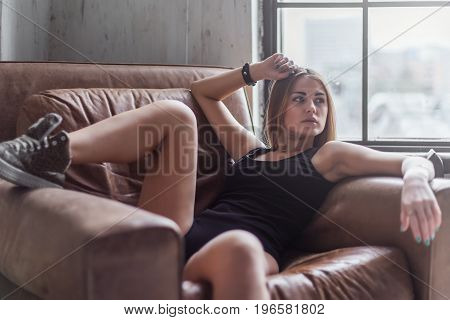 Sexy young woman relaxing reclining on a leather armchair in underwear and shoes in a room.