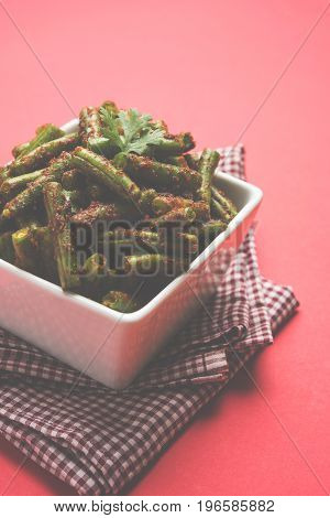 A Masala or fried vegetable dish consisting of green beans, onions, and curry spices, served in square bowl, selective focus