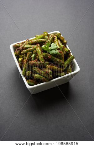 A Masala or fried vegetable dish consisting of green beans, onions, and curry spices, served in square bowl, selective focus