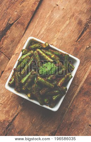 A Masala or fried vegetable dish consisting of green beans, onions, and curry spices, served in square bowl, selective focus