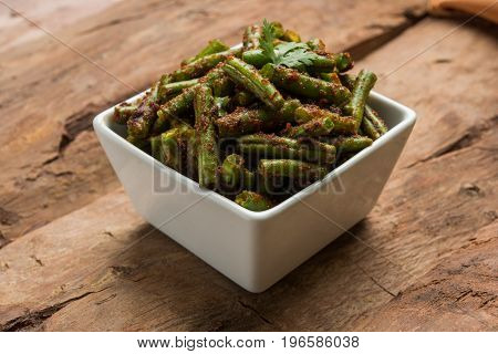 A Masala or fried vegetable dish consisting of green beans, onions, and curry spices, served in square bowl, selective focus