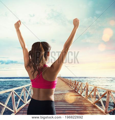 Girl stretches on a pier at sunset with sea landscape. Fitness, win and exultation concept