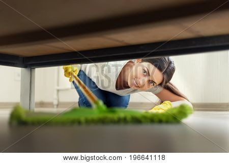 young woman in protective gloves cleaning floor under bed with mop. Housework, housekeeping and wet cleaning concept