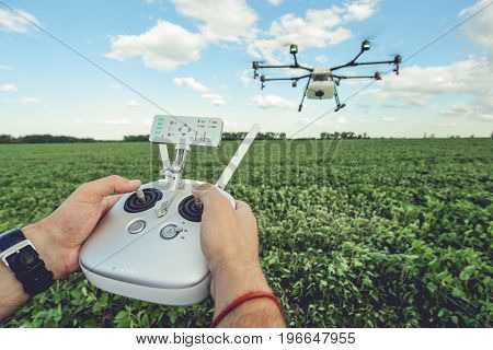 The man control octocopter or remote control for the drone in the hands for take a picture on sky. Agriculture drone flies over the green field.