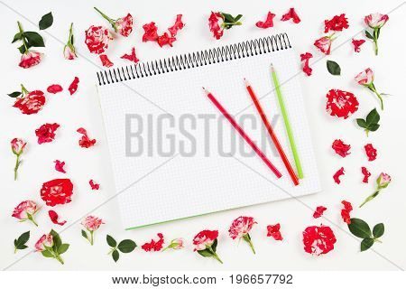 Open spiral notebook with colored pencils and flower frame on white background. Flat lay, top view