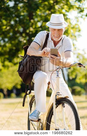 Write a message. Attractive mature man sitting on his transport and feeling happiness while reading answer from his friend