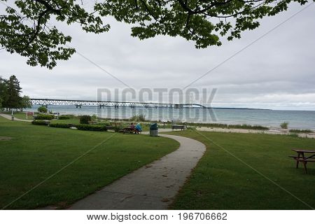 MACKINAW CITY, MICHIGAN / UNITED STATES - JUNE 18, 2017:  Visitors may sit in Alexander Henry Park, and enjoy the view of the Mackinac Bridge, which spans the Straits of Mackinac, to connect Michigan's Lower and Upper Peninsulas.