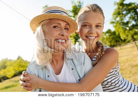 Express your love. Cheerful smiling young girl embracing her grandmother and expressing her emotions while resting together in the park