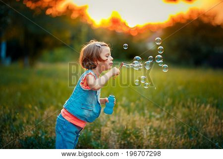 Five years old caucasian child girl blowing soap bubbles outdoor at sunset - happy carefree childhood