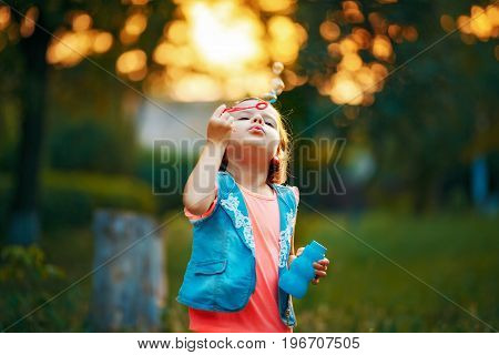 Five years old caucasian child girl blowing soap bubbles outdoor at sunset - happy carefree childhood