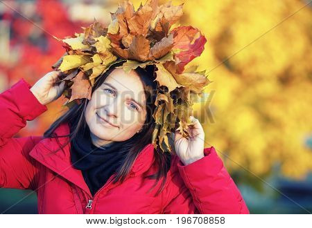 Pretty young woman with with a wreath of autumn maple leaves. Girl in autumn. Selective focus on model. Toned image.