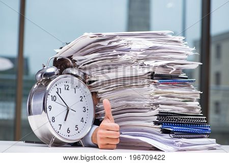 Businessman with pile stack of paper paperwork and an alarm cloc