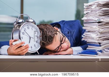 Businessman with pile stack of paper paperwork and an alarm cloc