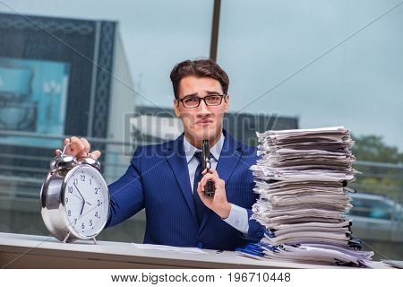Businessman with pile stack of paper paperwork and an alarm cloc