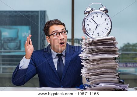 Businessman with pile stack of paper paperwork and an alarm cloc