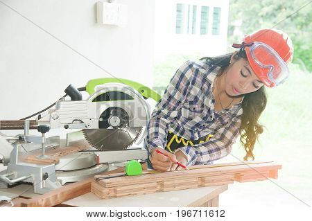 Pretty Asian carpenter woman is marking on wood for cut.