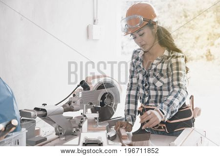 Pretty Asian carpenter woman is marking on wood for cut.