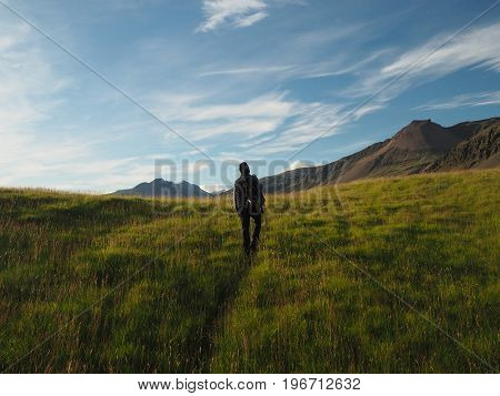 man walking with backpack through the meadow to the mountains with blue sky background