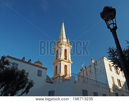 Churche tower in Calvi Corse France in golden light with lamp and blue sky background