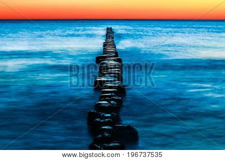 Wooden spur dykes in coastal sunset. Old groynes and wavy sea water, Baltic Sea, Island of Hiddensee, Germany.