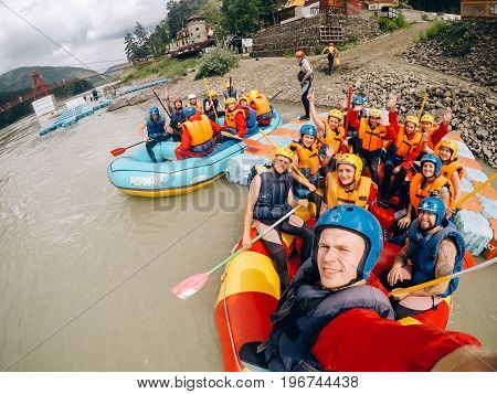mountain Altai, RUSSIA - July 16, 2017: man in a helmet holds an action camera and makes selfie on the background of friends with oars, rafting